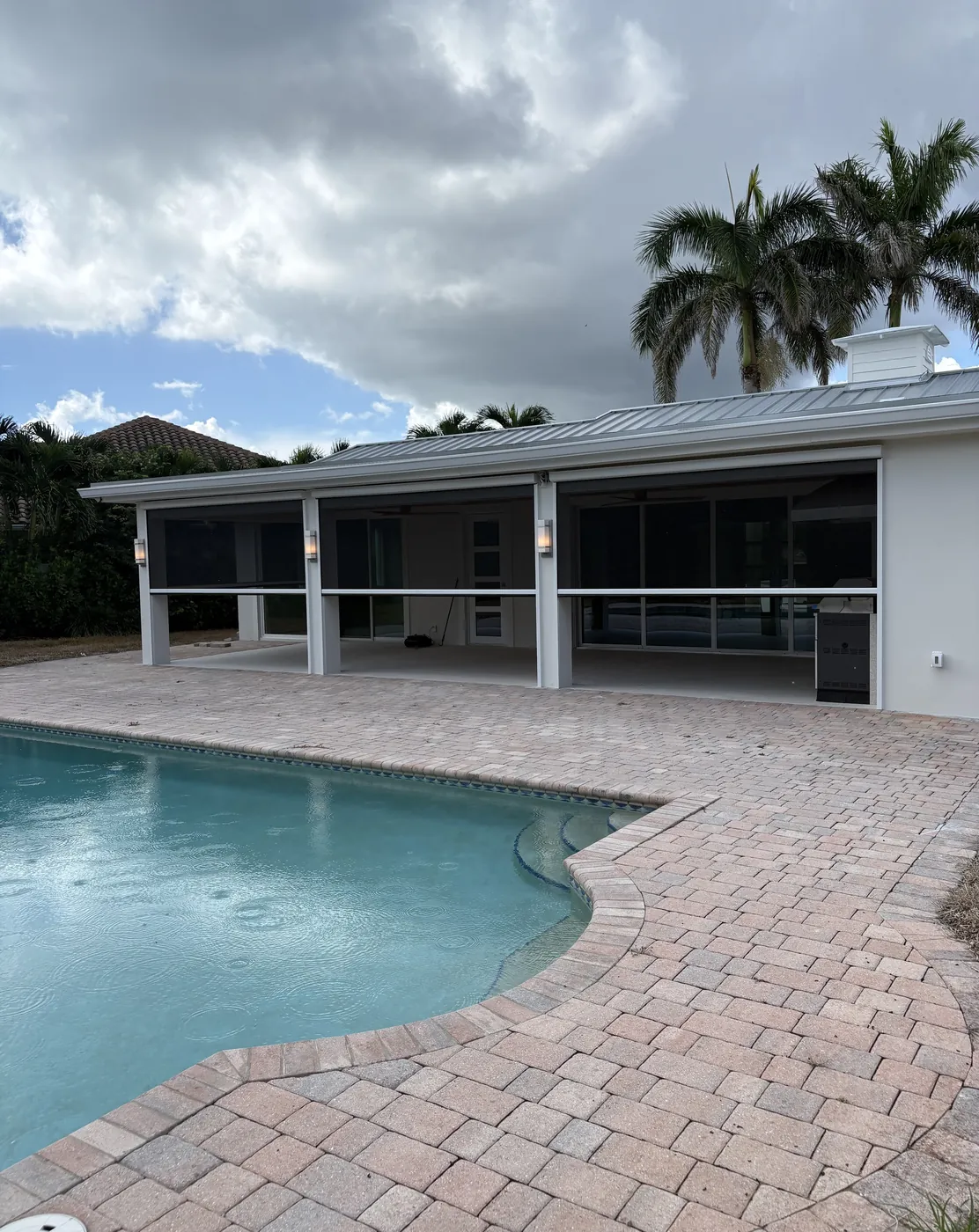 Poolside Patio with Motorized Screens and Paved Decking Under Cloudy Sky